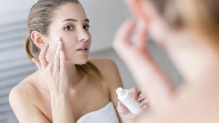 Woman applying cream on her face in a bathroom