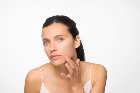 A woman examining her skin in the mirror as part of her clear skin routine